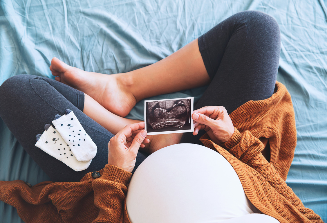 Femme enceinte vue du dessus assise en tailleur, regardant une photo de son échographie. Femme enceinte vue du dessus assise en tailleur, regardant une photo de son échographie.