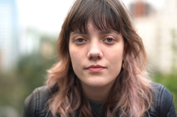 Jeune femme avec un frange, regardant l'objectif avec un léger sourire.