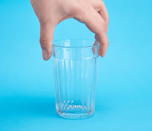 Une main adulte tenant un verre d'eau vide sur un fond bleu uni.
