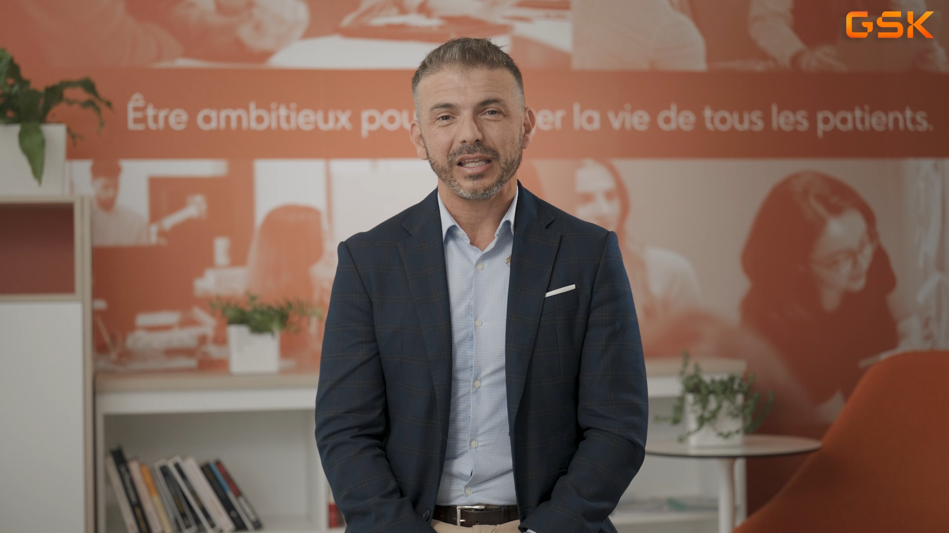 Femme aux cheveux courts bruns, portant un sweat à capuche vert, assise pour une interview vidéo avec logo aufeminin en haut à droite.