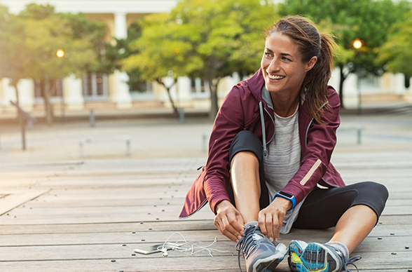 Jeune femme souriante, regard au loin vers la gauche, assise dans un parc, en train de refaire les lacets de ses chaussures de sport. Jeune femme souriante, regard au loin vers la gauche, assise dans un parc, en train de refaire les lacets de ses chaussures de sport.