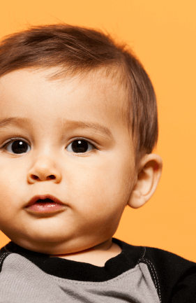 Portrait d'un bébé avec des yeux noisette et un body noir et gris, sur un fond orange uni.