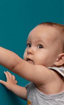 Bébé curieux pointant du doigt vers une prise murale sur un mur bleu.