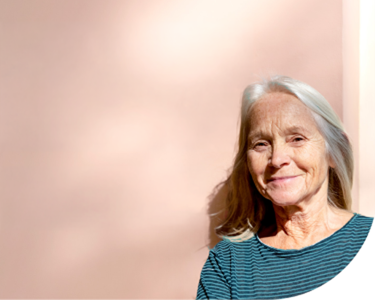 Portrait d'une femme âgée souriante sur un fond beige clair avec espace pour texte à gauche.