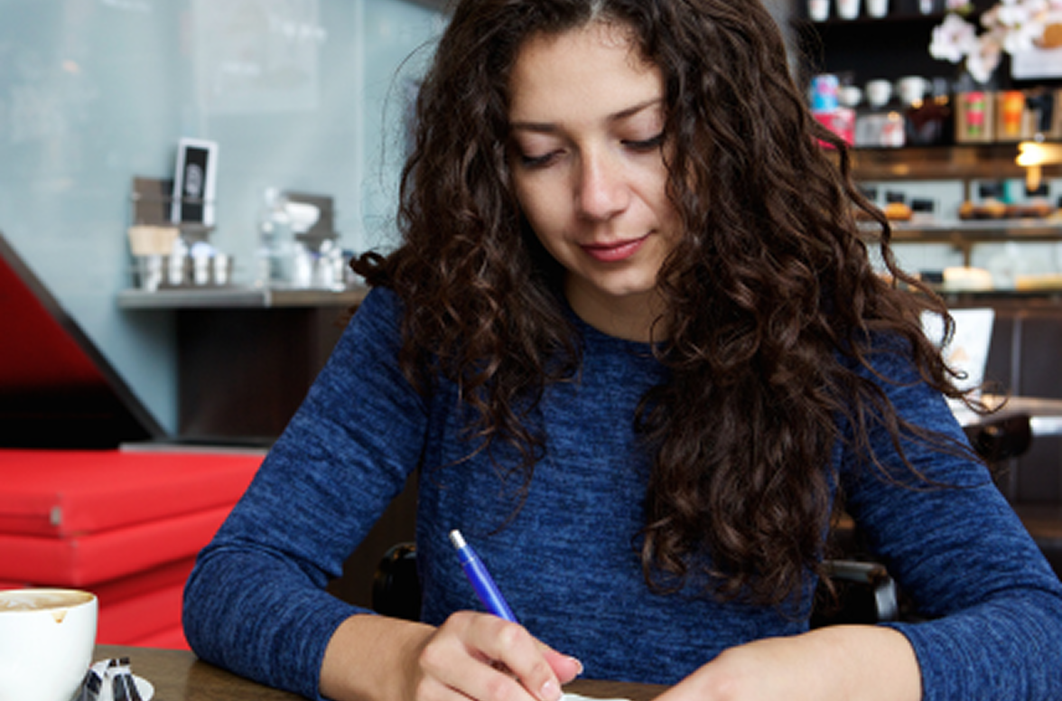Jeune étudiante brune aux cheveux longs et bouclés avec un haut bleu, esquissant un léger sourire et prenant des notes. Jeune étudiante brune aux cheveux longs et bouclés avec un haut bleu, esquissant un léger sourire et prenant des notes.