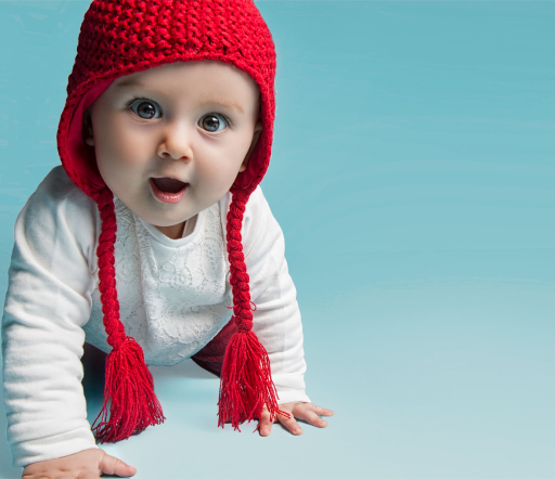 Un bébé avec un bonnet rouge marche à quatre pattes.