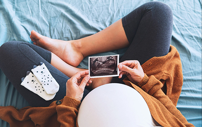 Femme enceinte vue du dessus assise en tailleur, regardant une photo de son échographie.