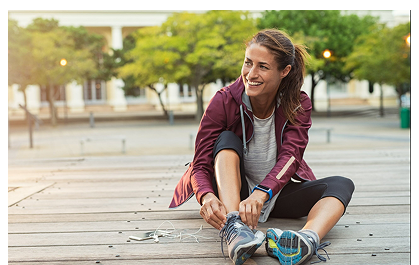 Jeune femme souriante, regard au loin vers la gauche, assise dans un parc, en train de refaire les lacets de ses chaussures de sport.